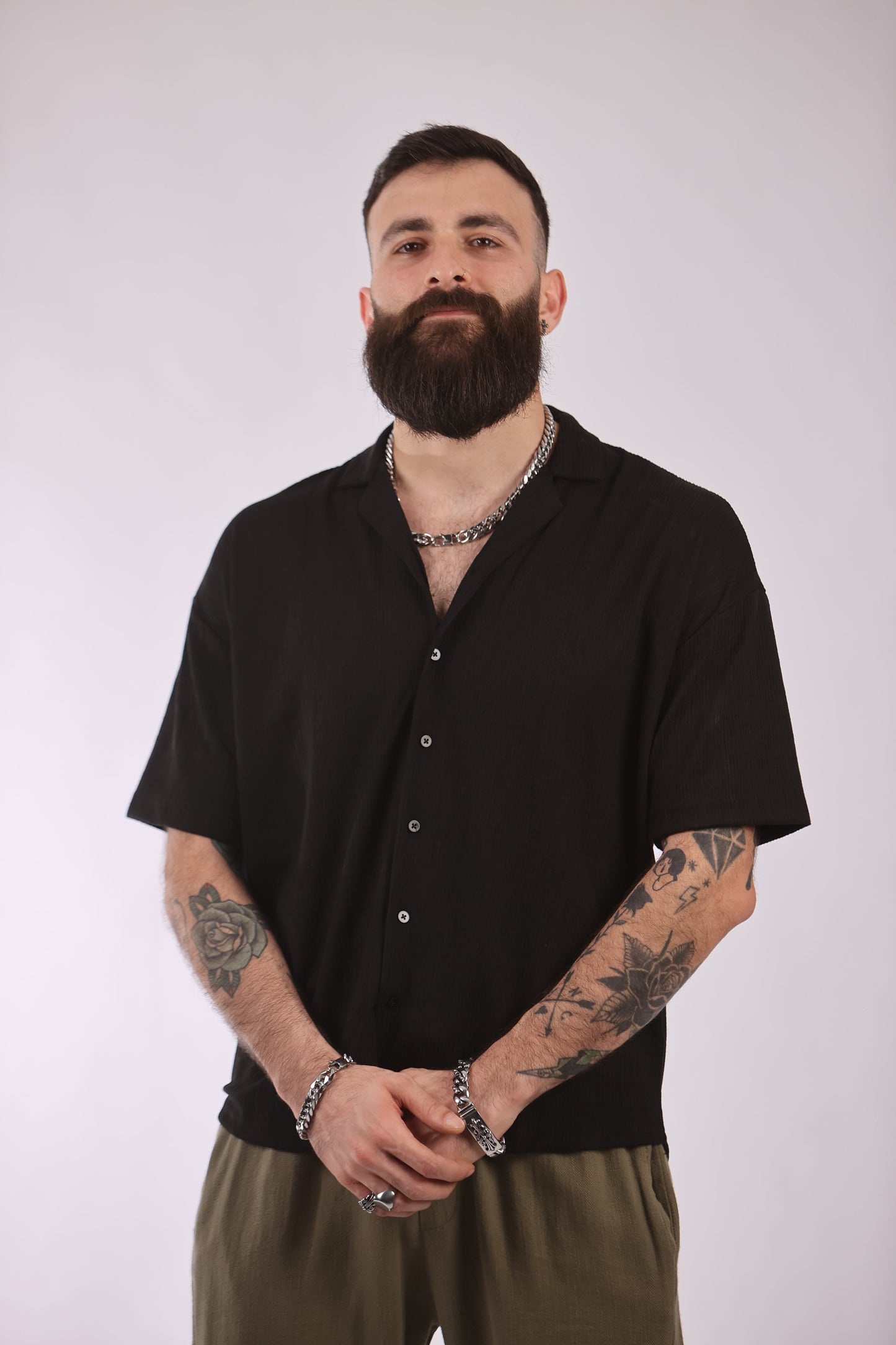 Man wearing black Marrakech shirt with short sleeves and button-up front, showcasing tattoos and jewelry.
