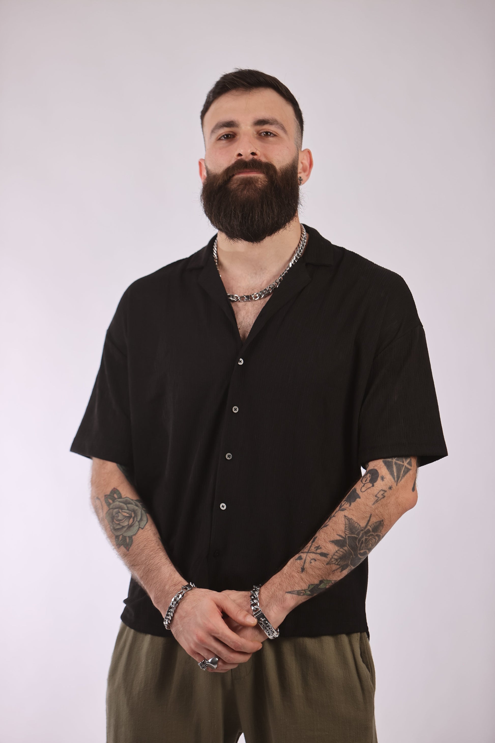 Man wearing black Marrakech shirt with short sleeves and button-up front, showcasing tattoos and jewelry.